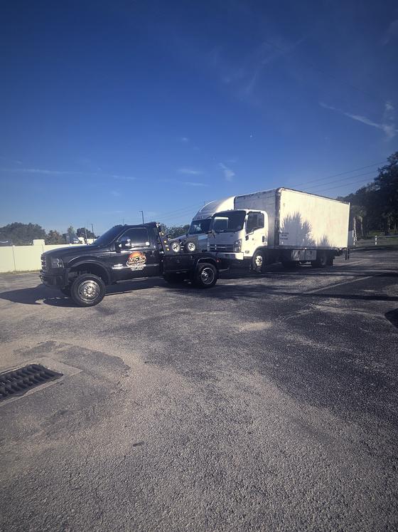 A white box truck hooked to Vic's wrecker in a commercial yard.