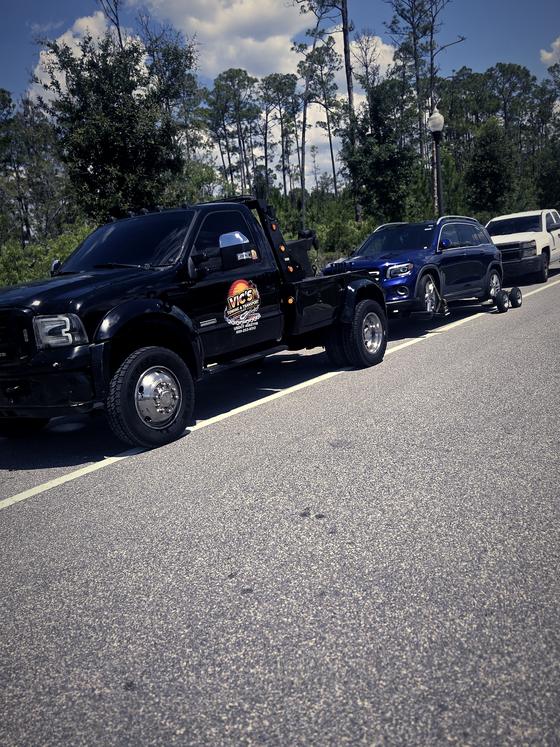 A blue Mercedes GLB lifted onto dollies behind Vic's wrecker.