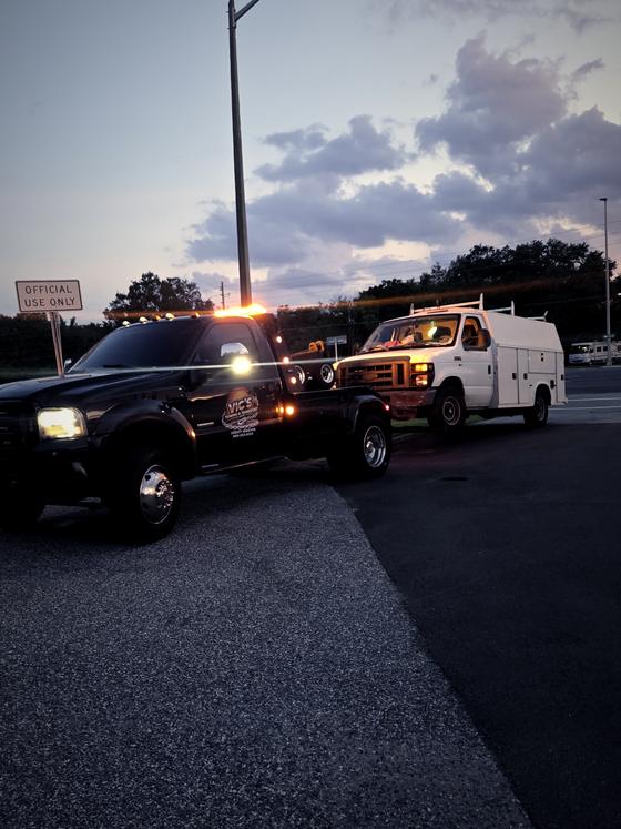 Vic's wrecker with strobes lit at dusk towing a utility service truck.