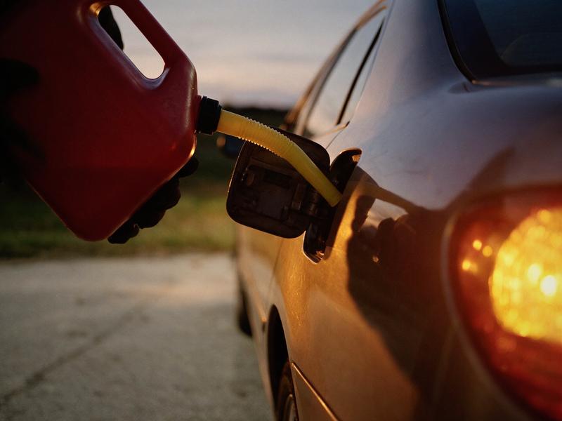 A red fuel can being poured into a car's open filler neck at dusk.