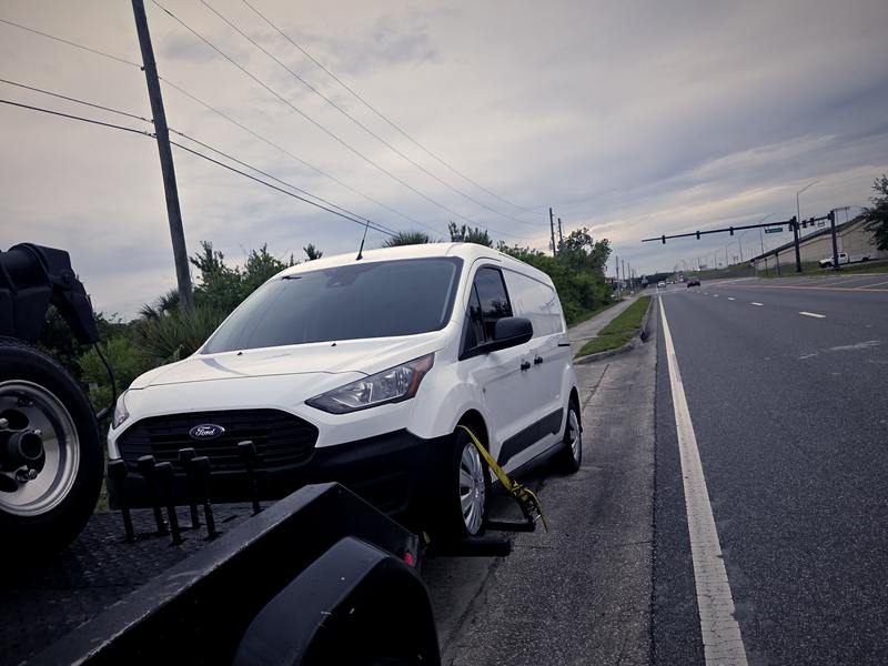 A van secured on a flatbed with a timestamped job record overlaid.