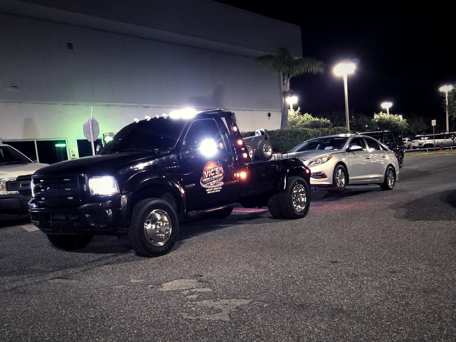 A silver sedan being removed from a retail lot at night.