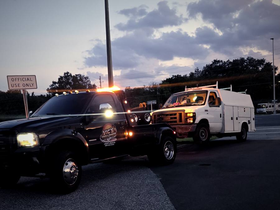 Vic's wrecker with amber strobes lit beside a white utility truck.